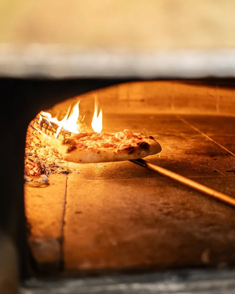 Pizza op de schep voor het vuur van de oven